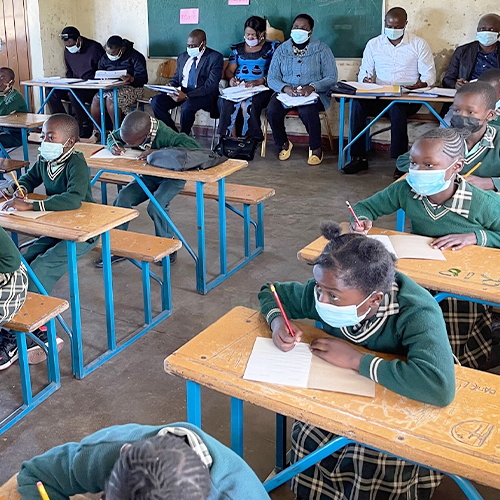 "Young students in a classroom in Zambia sitting at their desks writing into notebooks"