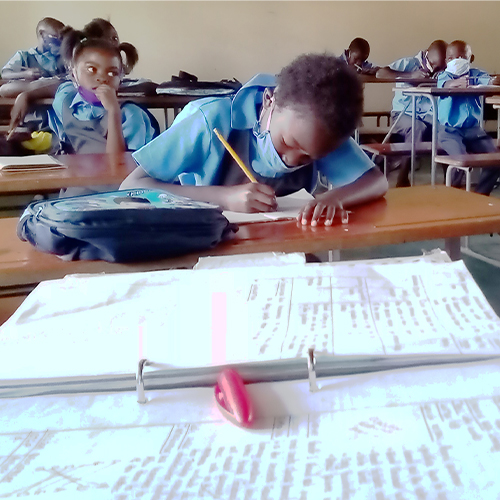 "Children in Zambia in a classroom writing in notebooks. There is an open three -ring binder containing notes in the foreground of the photo."