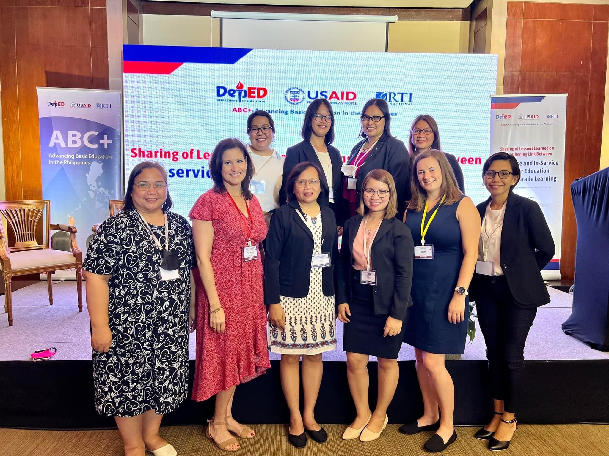 "Group photo in front of a digital backdrop with logos of DepEd, USAID and RTI.""