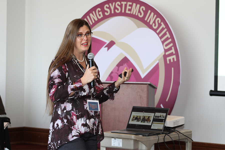 "Dr. Adrienne Barnes-Story with a microphone presenting in front of a large LSI logo banner."