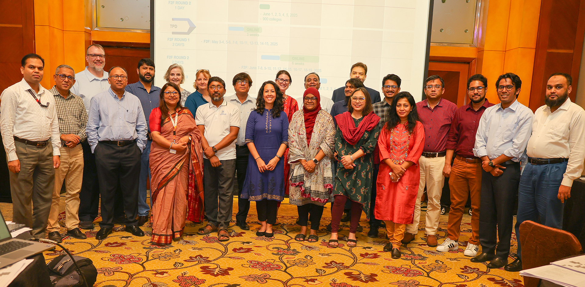 "Group photo in a hotel conference room in Bangladesh in front of a large projection screen."