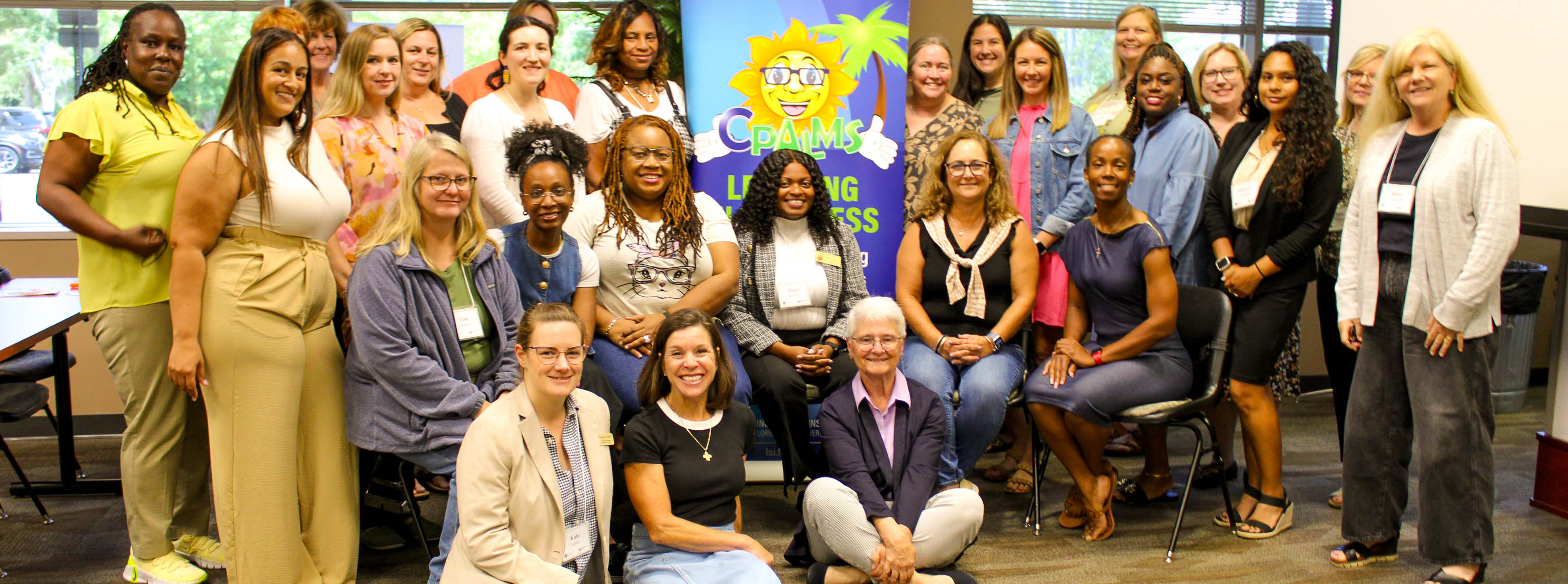 Group photo of participants in an ELA assessment writing workshop posing in front of a stand-up banner for CPALMS.