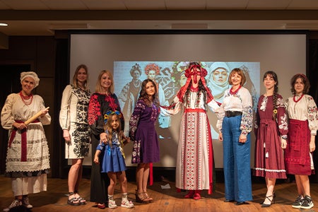 A group of women on stage in front of a projection screen modeling vyshyvankas at a Vyshyvanka Day celebration.