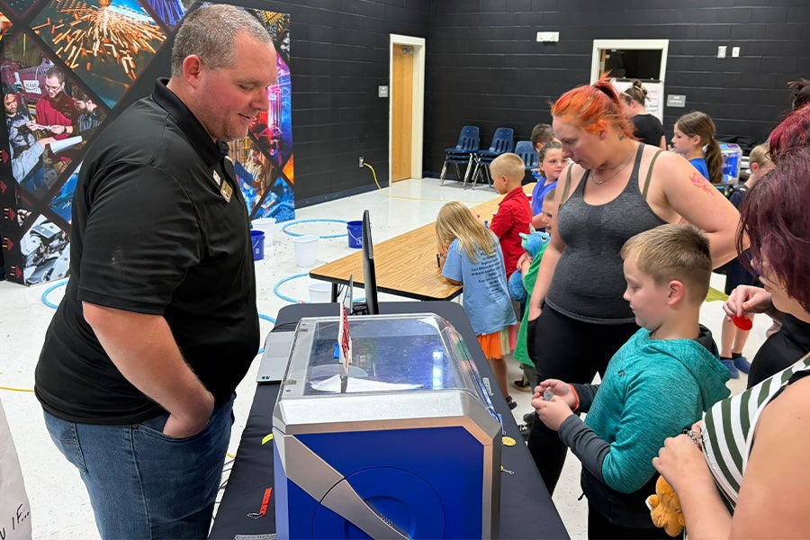 Robert Hanna talking with students and parents next to a 3D printer at a STEM night event.