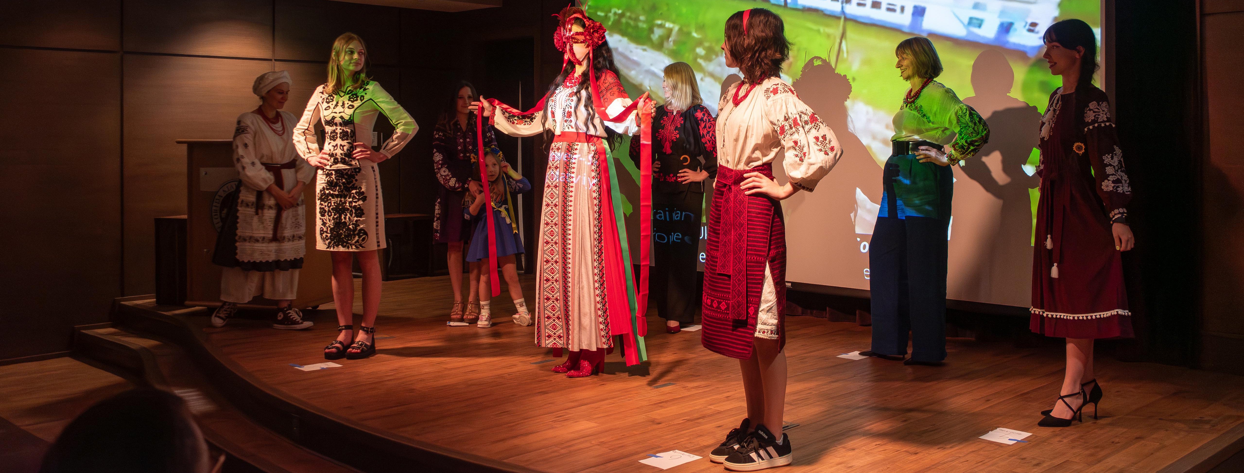 A group of women on stage in front of a projection screen modeling vyshyvankas at a Vyshyvanka Day celebration.