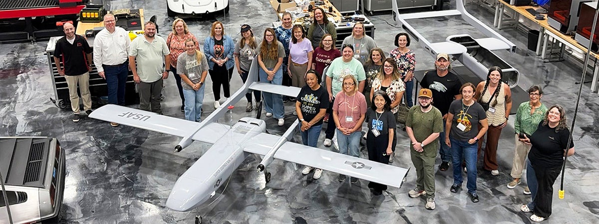 Group photo standing around an unmaned aircraft inside a warehouse. 