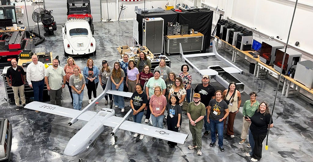 Group of InSPIRE participants at a warehouse gathered around a large drone for a group photo.