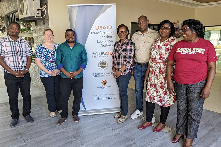 Stephanie Simmons Zuilkowski posing with a group in Zambia in front of a sign.