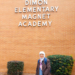 Dr. Ely photo outside in front of a brick wall with a sign for Dimon Elementary School.