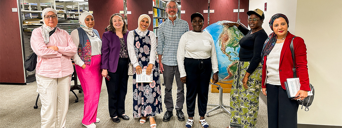 "Egyptian fellows posing for a photo with two FSU employees and two Zambian fellows in front of stacks of books."