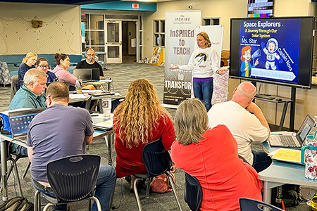 Classroom of educators watching a presentation on a flat screen TV.