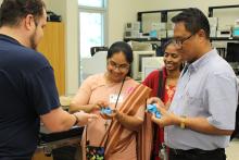Three members of the India CCAP Group in a classroom with a a presenter. Two are holding small plastic puzzles