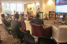 A small group sitting in chairs listening to a man talking with a microphone