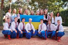 Group photo of people wearing vyshyvankas posing around a Ukrainian flag. 