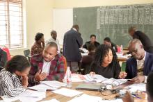 Teacher training in a room with people sitting around tables in discussion.