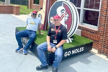 Dmytro Diadin, Ph.D. and Oleksandra Hrytstna, Ph.D. stiing at the FSU softball sdtadium in front of a large Seminole head FSU logo.