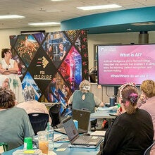 LSI's Carrie Meyers conducting an AI in education session standing next to a flat screen TV.