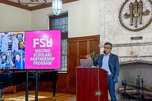 Farrukh Alvi standing at a podium next to a digital display with the logo for FSU's Visiting Scholar Partnership Program.