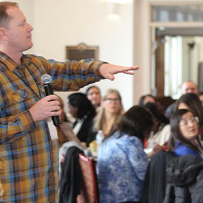 Dr. Rob Schoen holding a microphone presenting to a crowd at an LSI meeting. 