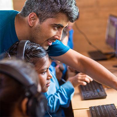 Bhushan Dahal working with children in front of a computer screen.