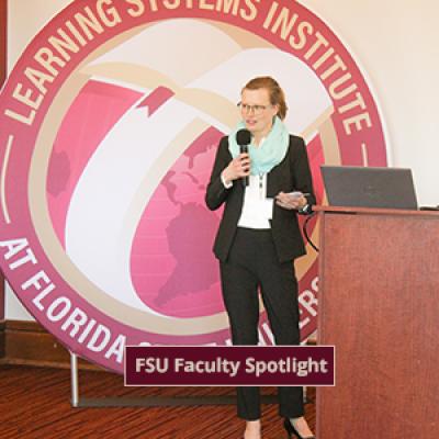 Celia Reddick addressing the LSI staff in front of a large round LSI logo banner.