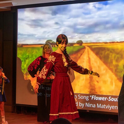 Woman on stage in front of a projection screen modeling a vyshyvanka at a Vyshyvanka Day celebration.