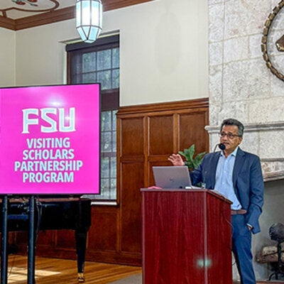 Farrukh Alvi standing at a podium next to a digital display with the logo for FSU's Visiting Scholar Partnership Program.