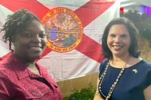 Two women pose in front of the State of Florida flag