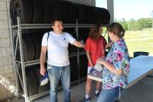 Three people outside in front of a rack of vehicle tires
