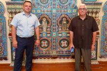 Two men posing in front of a large religious mosaic