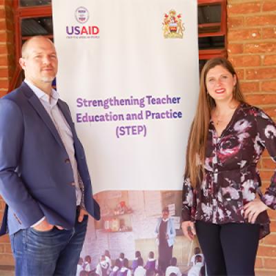 Jeremy Koch and Dr. Barnes-Story posing next to a banner for the USAID funded STEP project in Malawi. 