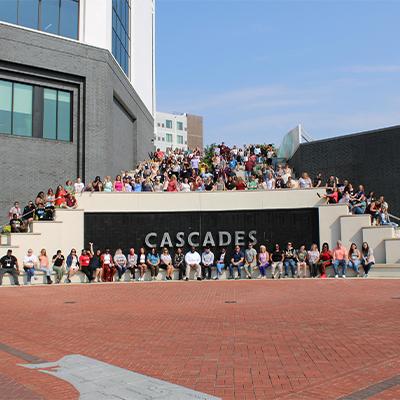 Group photo of 100+ people surrounding a large sign for Cascades Park