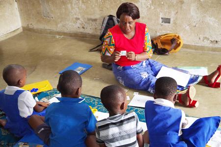 Educator in a classroom in Malawi sitting on the floor with children in front of her.