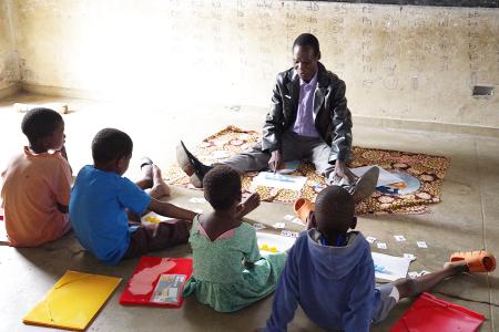 Educator in a classroom in Malawi sitting on the floor with children in front of him. 