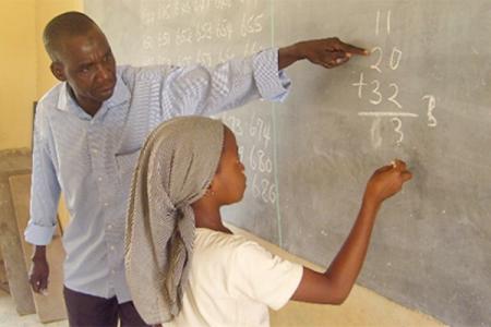 A young student at a chalk board being instructed by teacher.